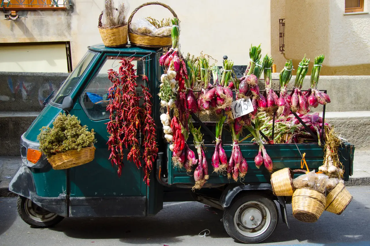 Old Italian tricycle with fresh produce hanging from it, showcasing traditional Italian farming in Le Marche.